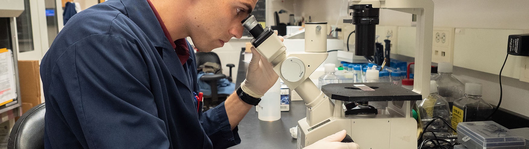 student in lab coat peering through microscope